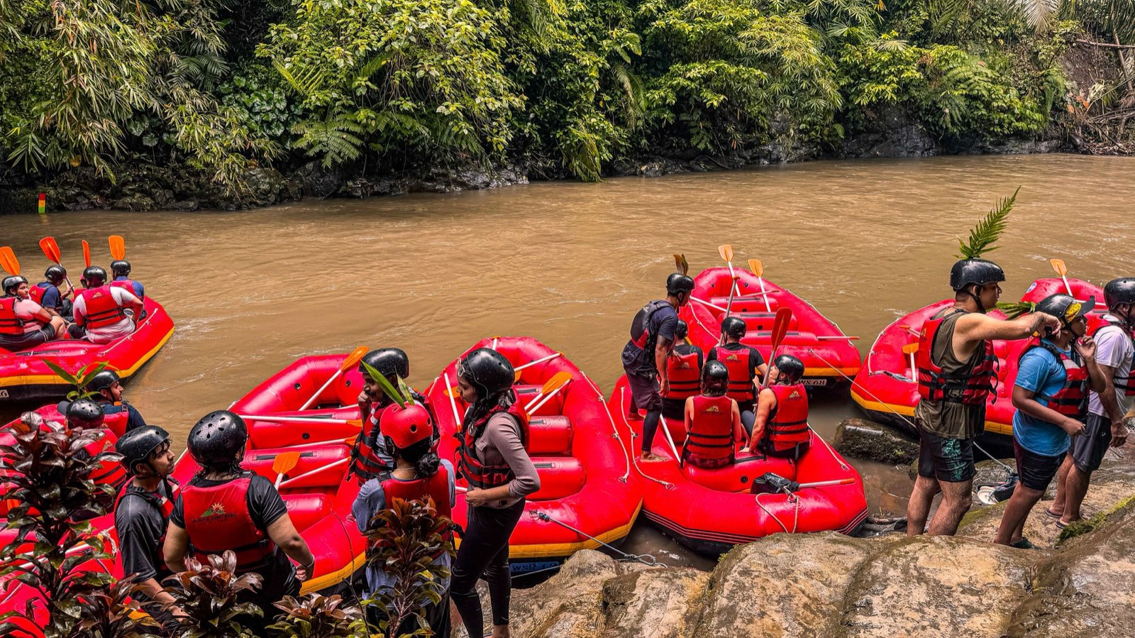 Red rafts on a river running between dense green banks.