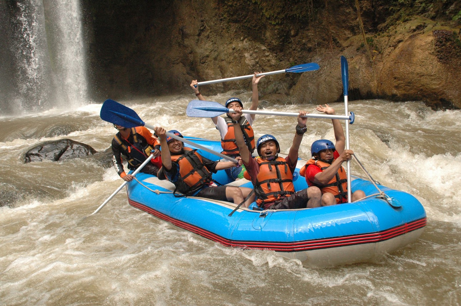 A raft dropping through rapids below a waterfall.