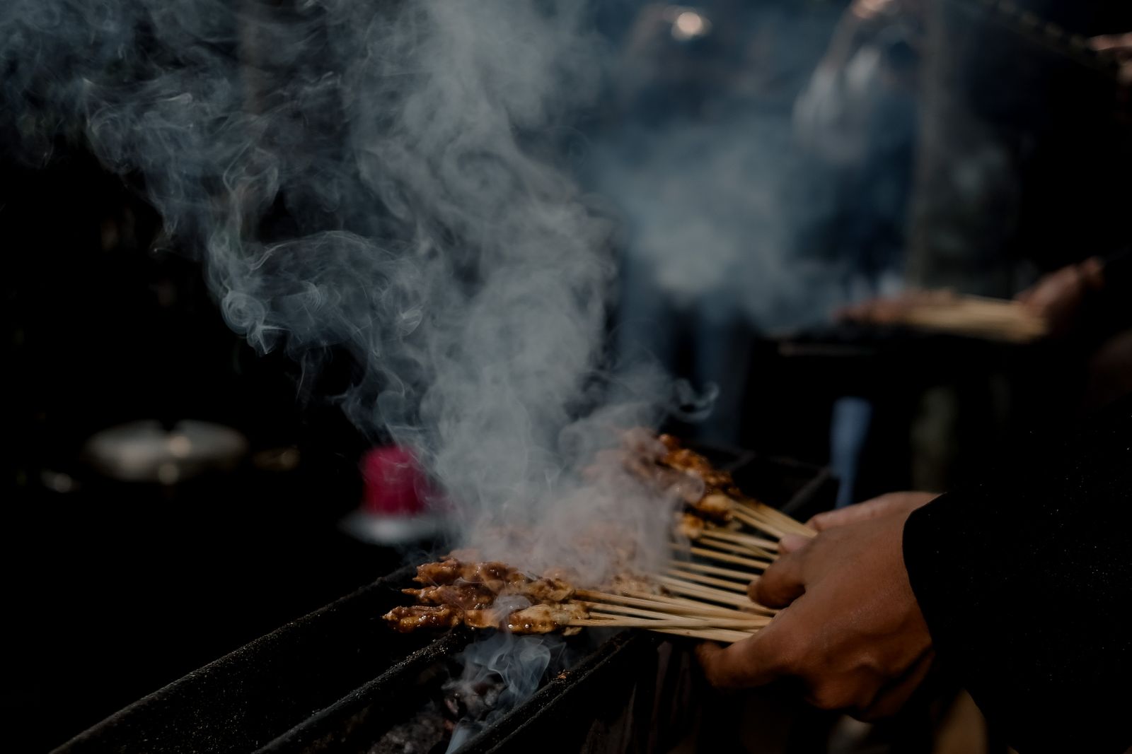 Satay skewers grilling over charcoal at a street market in Indonesia.