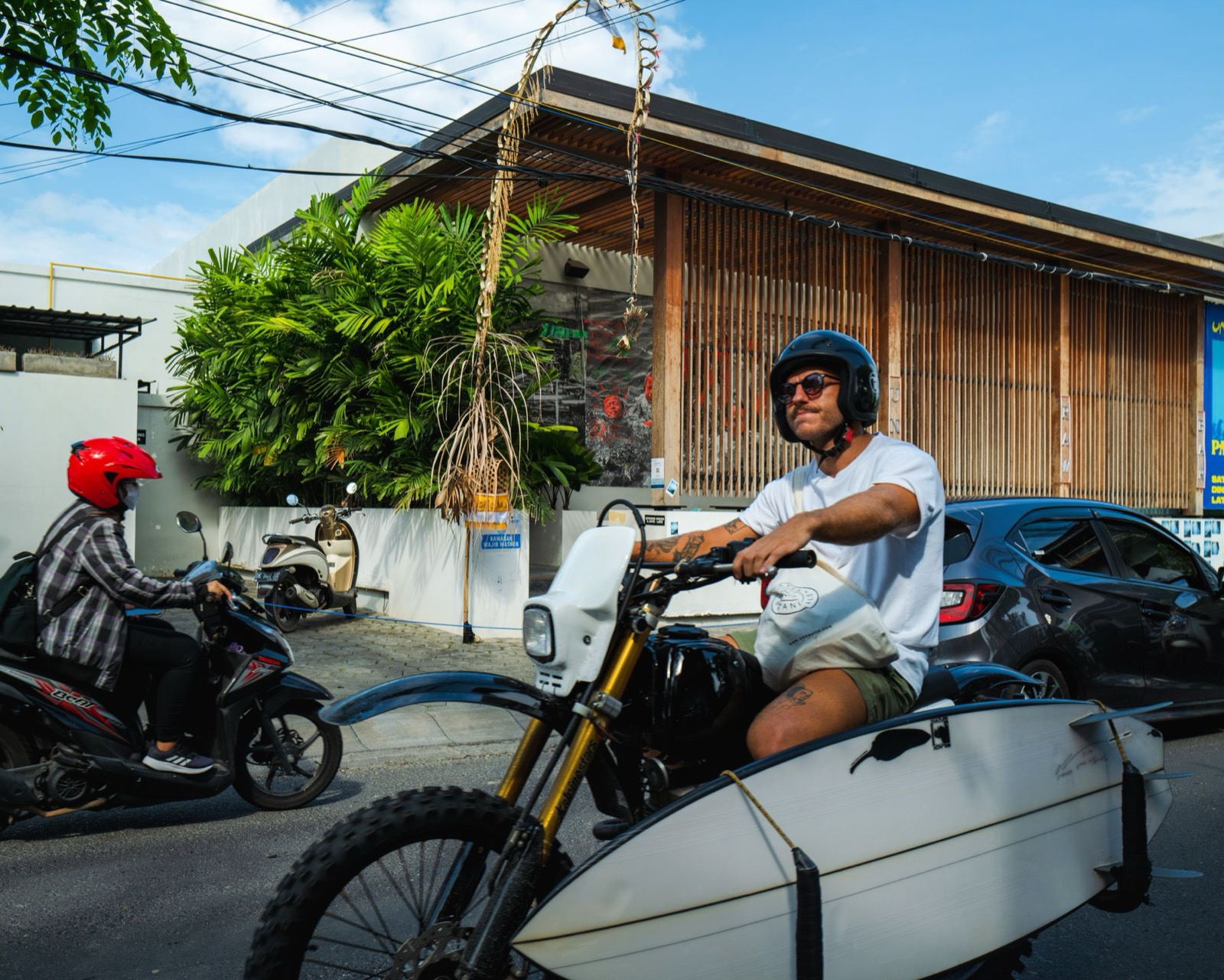 A rider carrying a surfboard on a motorbike in Bali.