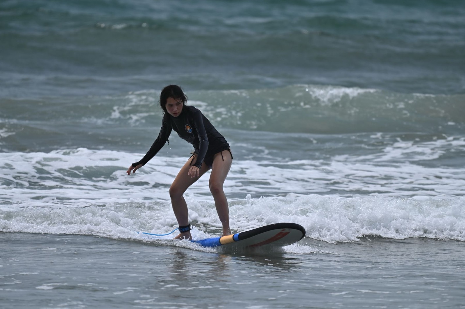 A surfer riding a small wave at a beach in Bali.
